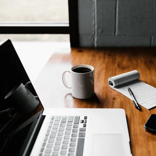 Computer on a table with a phone, notebook, and coffee>
